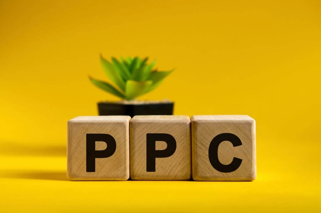 wooden blocks saying PPC with yellow background and a plant in the background